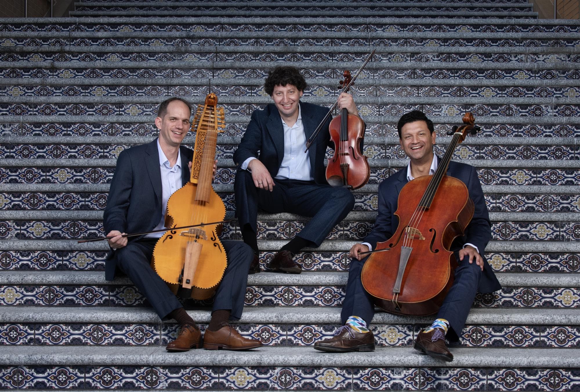 The trio seated across a tiled staircase, the baryton, viola and cello held across their laps.